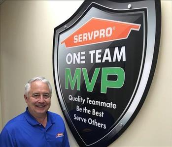 A man in a blue shirt standing in front of SERVPRO sign